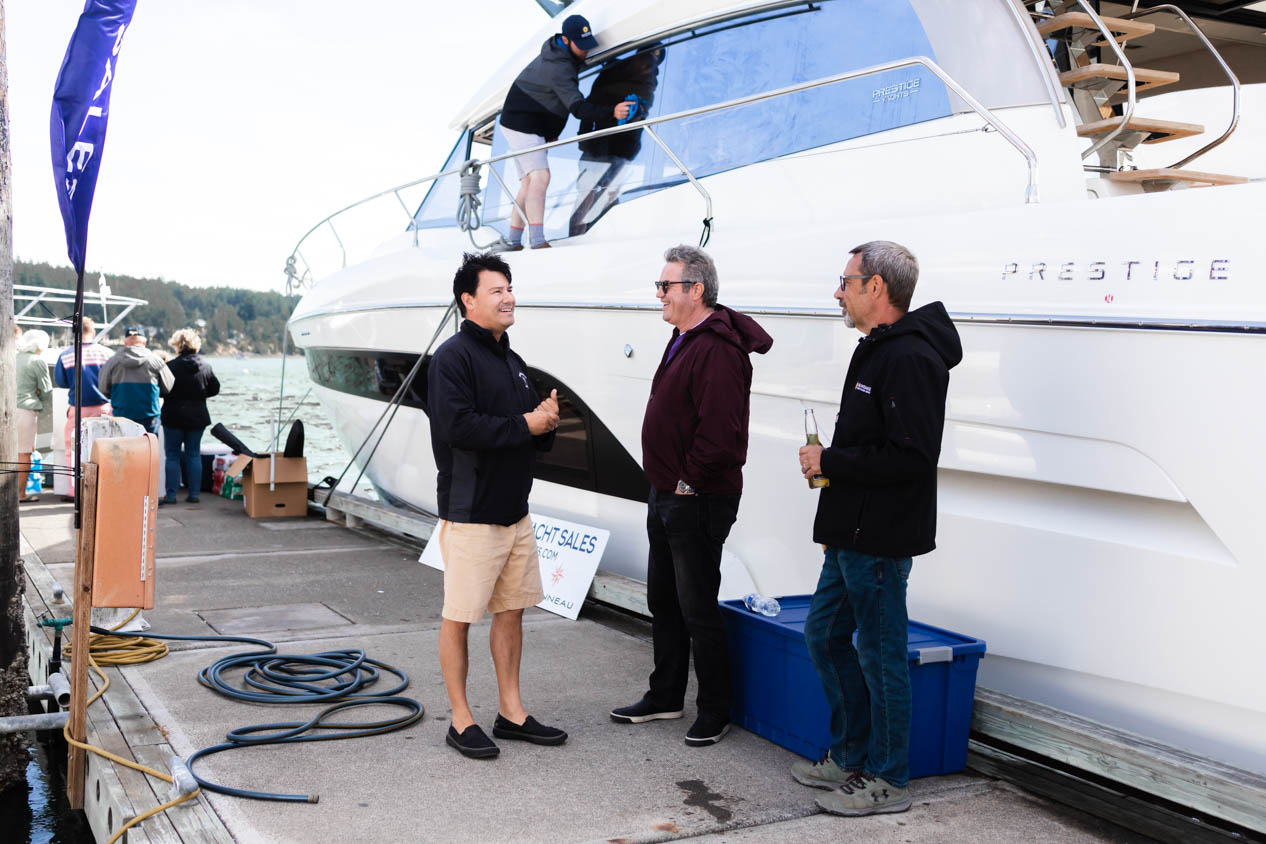 Three men smiling while talking on the dock in front of a Prestige Yachts 630