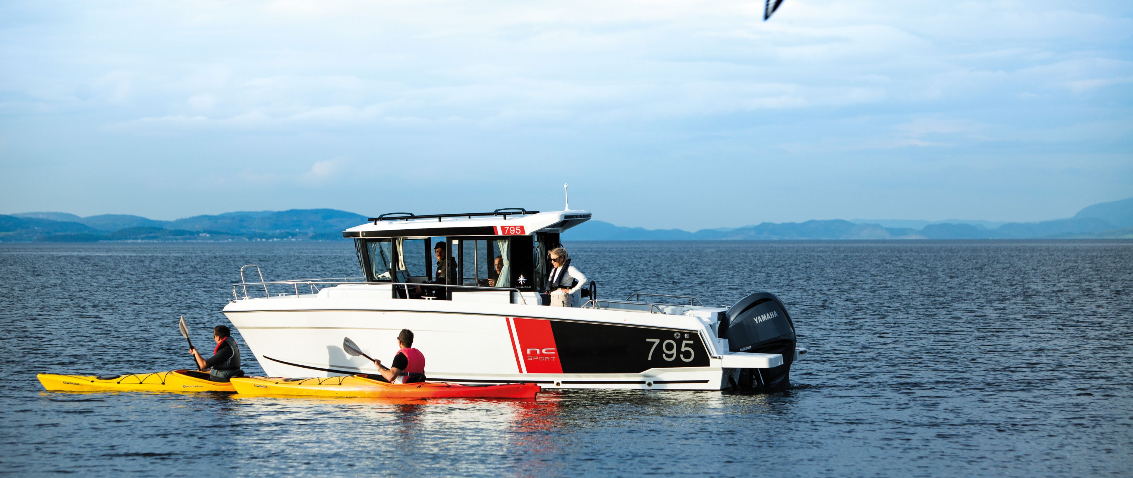 Jeanneau 795 Sport with two kayakers paddling by in open water