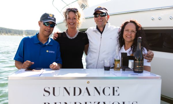 Four please standing behind a "Sundance Rendezvous" sign on a dock by a yacht