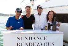 Four please standing behind a "Sundance Rendezvous" sign on a dock by a yacht