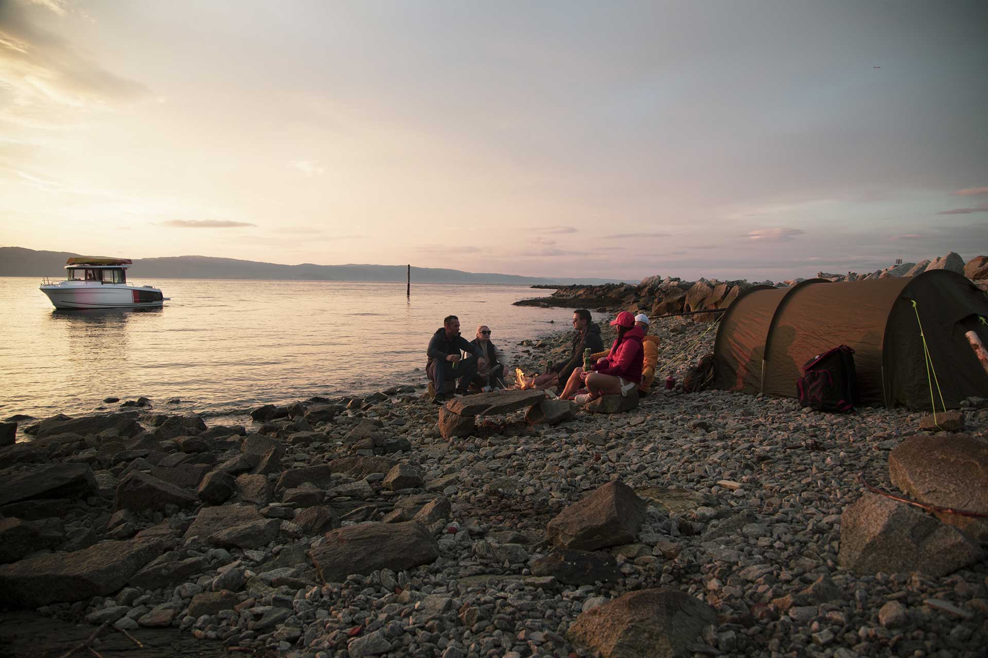 People camping on a beach with a boat in the background at sunset